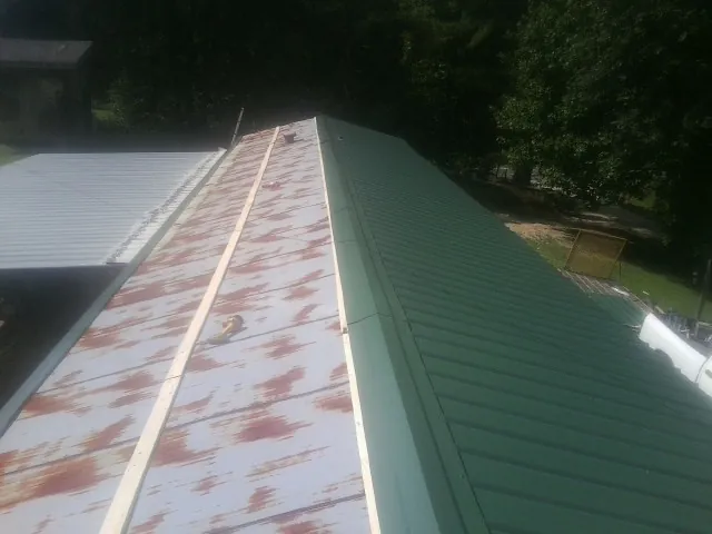 Old rusted panels beside newly installed green metal roofing — Wind Damage Roof Repair by Roofing Brothers in Providence