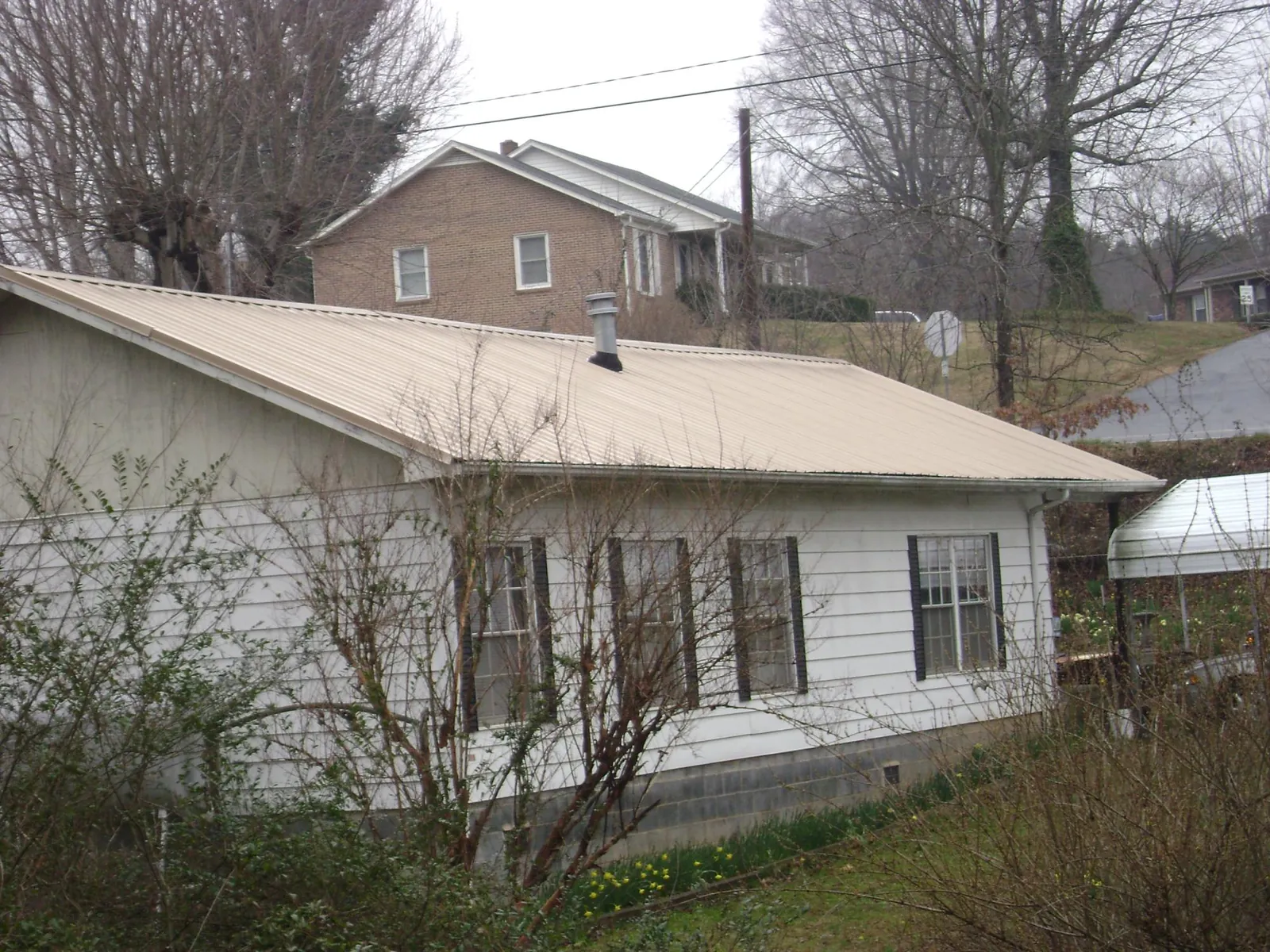 Tan metal roof on a white sided house set into a hillside — Commercial Roofing by Roofing Brothers in Providence